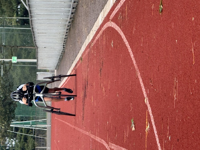 A frame runner mid-stride on an athletics track, leaning forward into the body support with feet pushing off the ground