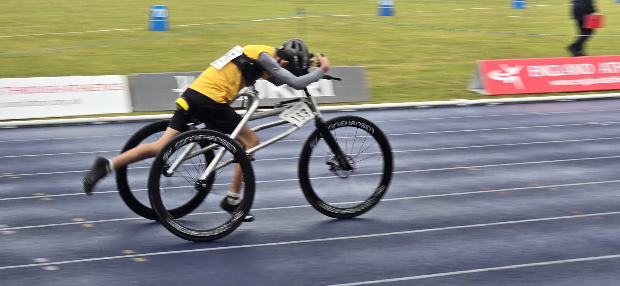 A young frame runner leaning forward at speed on an athletics track during a race, frame branded Connie Hansen